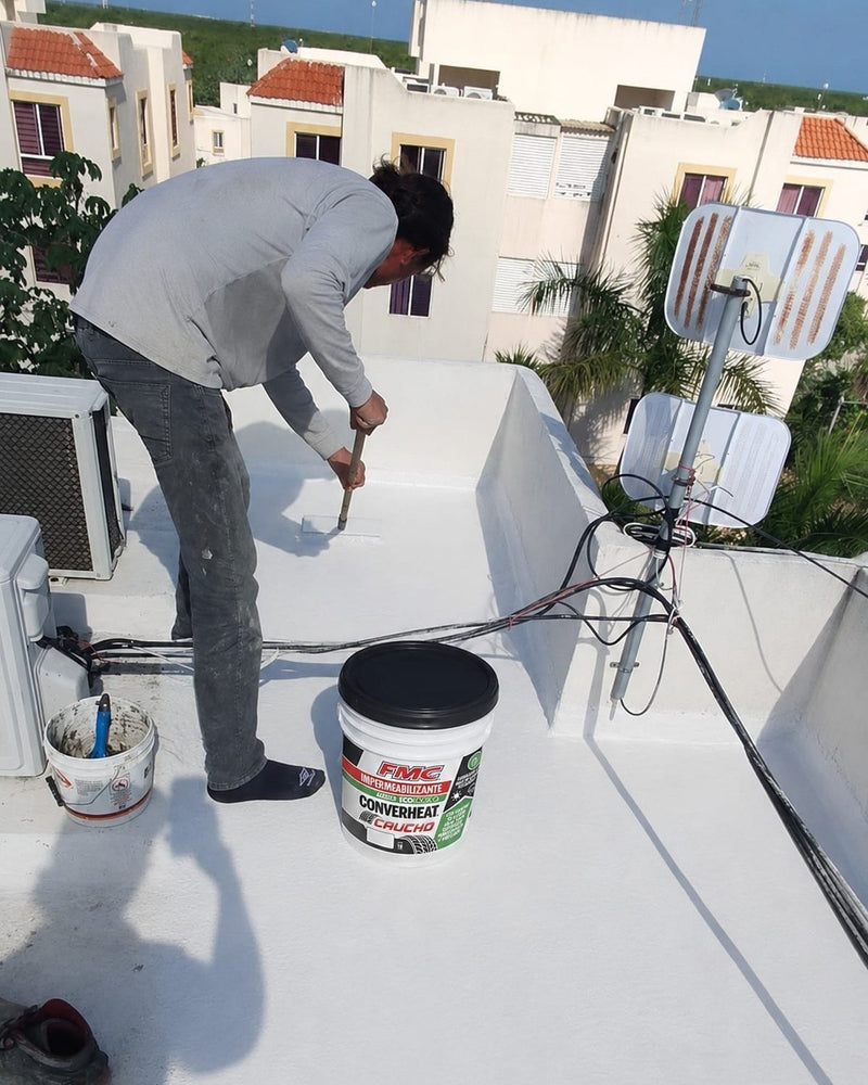 Aplicador de PYASE extendiendo Converheat Caucho con cepillo de ixtle sobre una losa de azotea en Cancún, con la cubeta de FMC a un costado